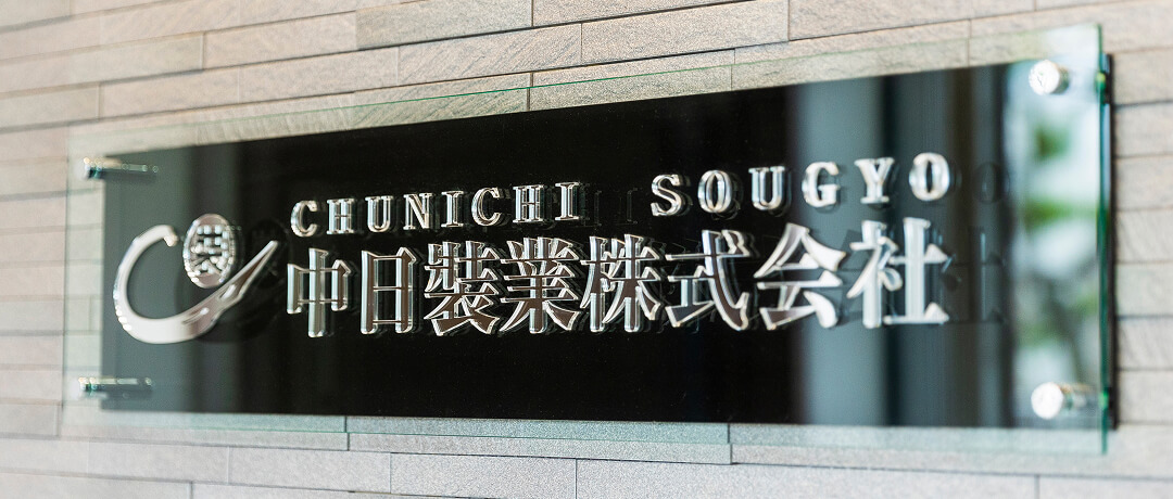 石張り壁面に中日裝業株式会社のロゴと社名のガラス看板が掲示されている様子