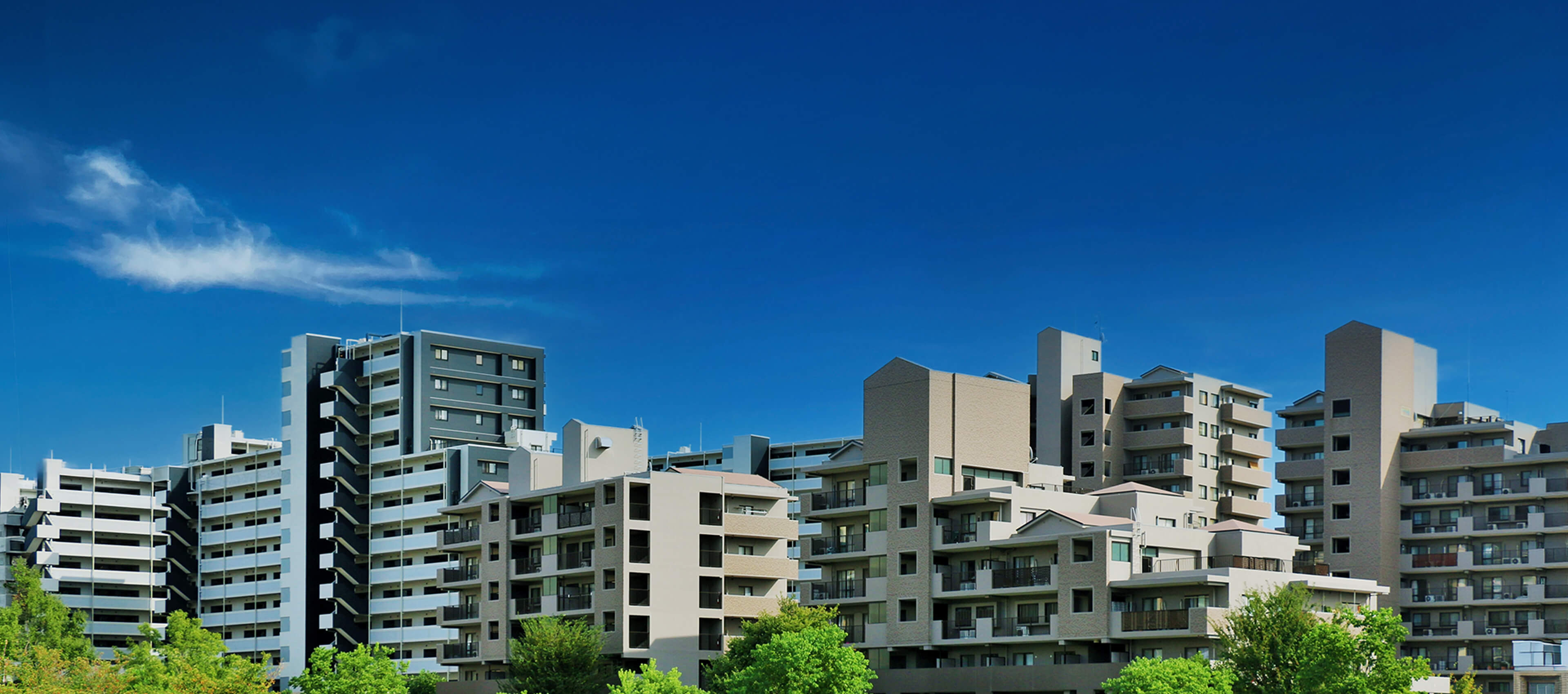 青空の下に複数の中高層マンションが立ち並ぶ住宅エリアの全景が広がる様子