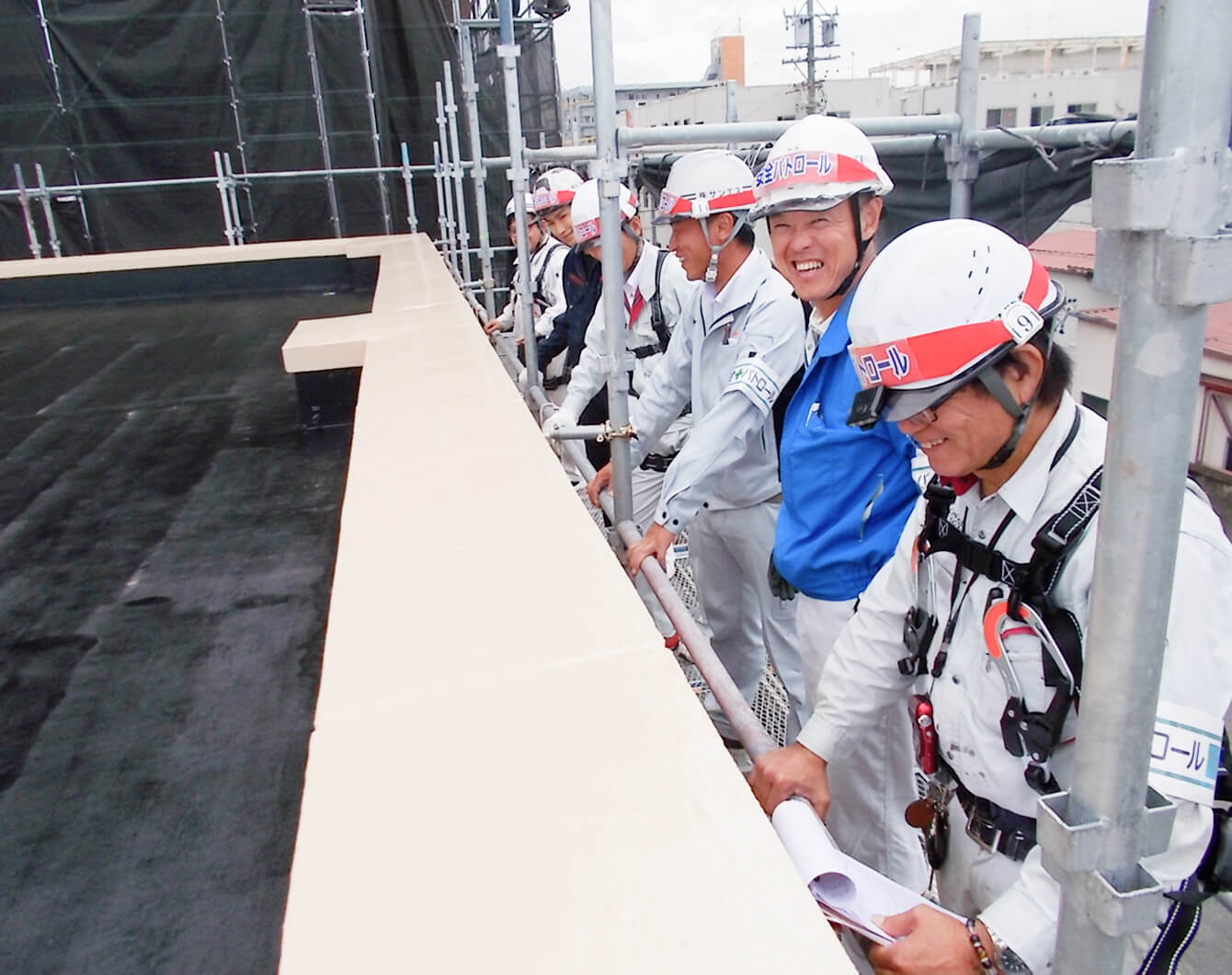 屋上修繕現場で、ヘルメットをかぶった作業員が足場に並んで立っている様子